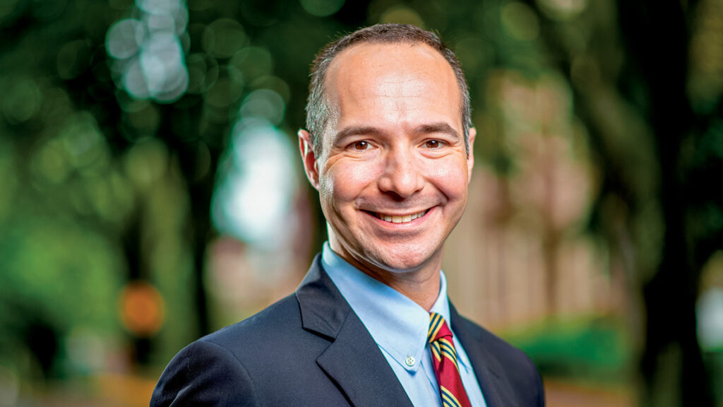 Brian Samble wears suit and red tie and smiles