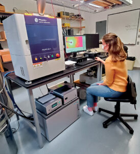 student sits in a lab with sophisticated machinery and computers
