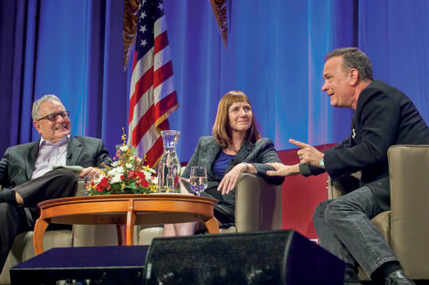 President Alison Byerly smiles as Tom Hanks talks on stage, Donald Miller sits with her