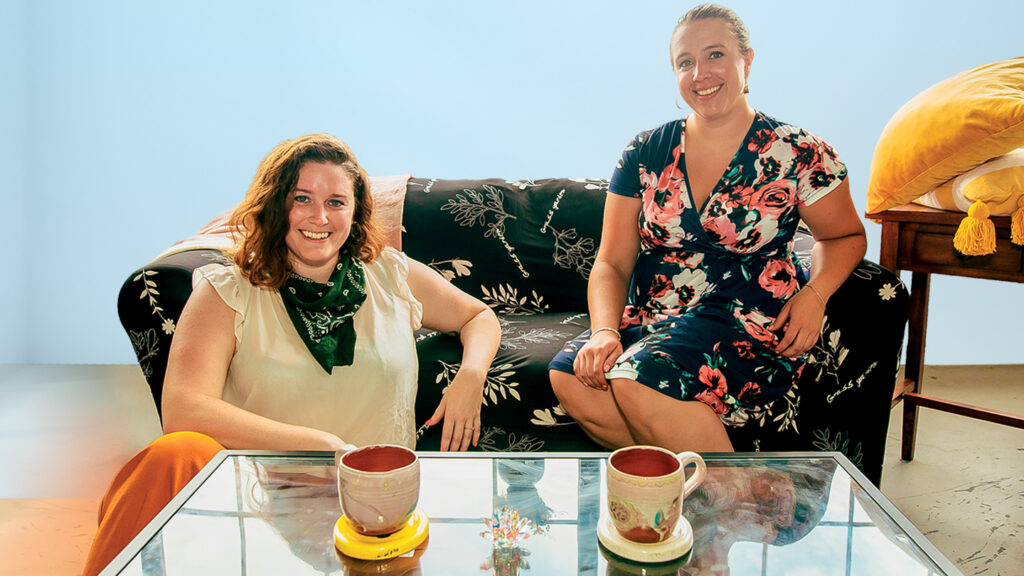 April Hinkle and Caitlin Flood ‘12 sit in a living room they furnished 