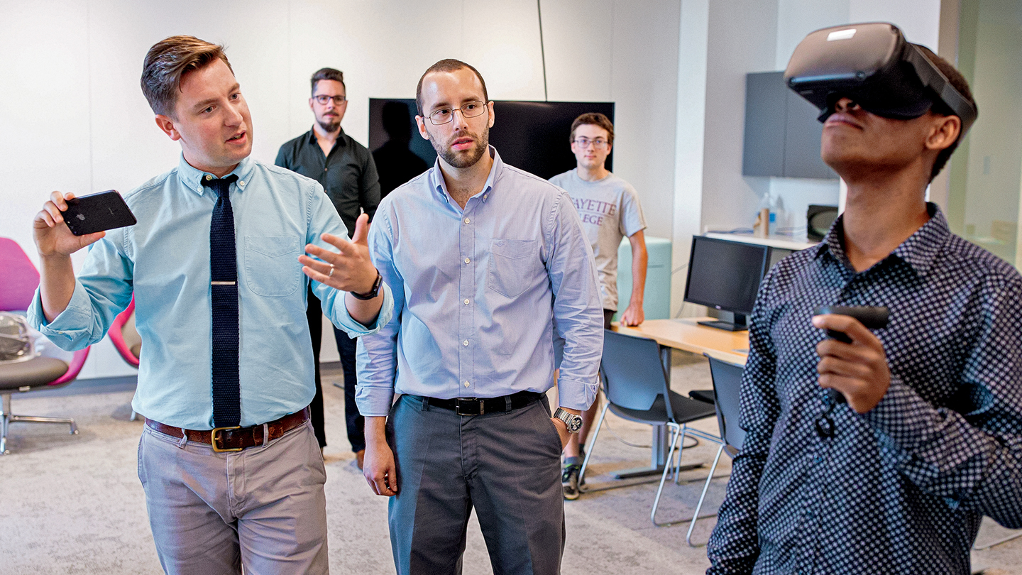 Profs. Eric Hupe (left) and Christian Lopez demonstrate the use of virtual reality with a student wearing a headset