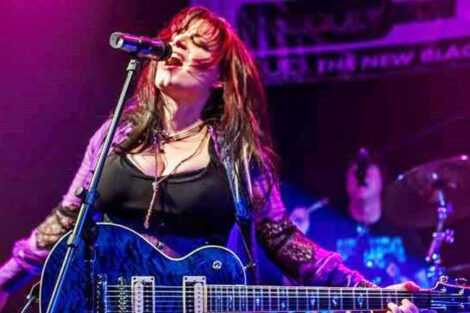 Dawn Botti sings into microphone on stage with a guitar around her neck