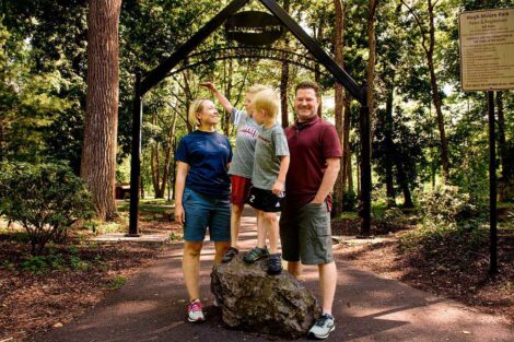 Lauren and Chris Anderson stand with their boys, who are standing on a rock, in front of the entrance to Hugh Moore Park